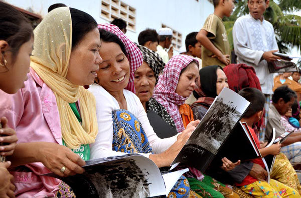 Women in colorful clothes sit together and read a book. 