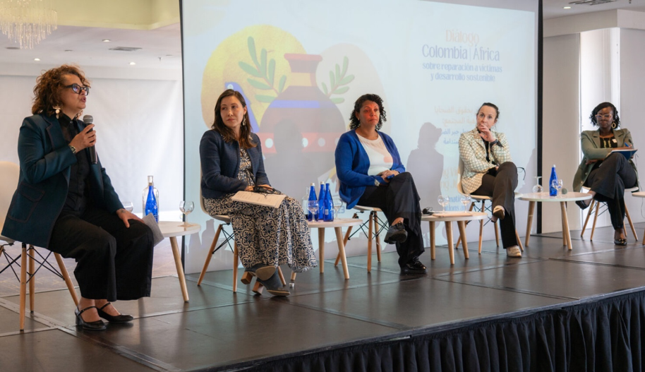 Cinco mujeres sentadas en el escenario. Una mujer habla, las demás la miran.