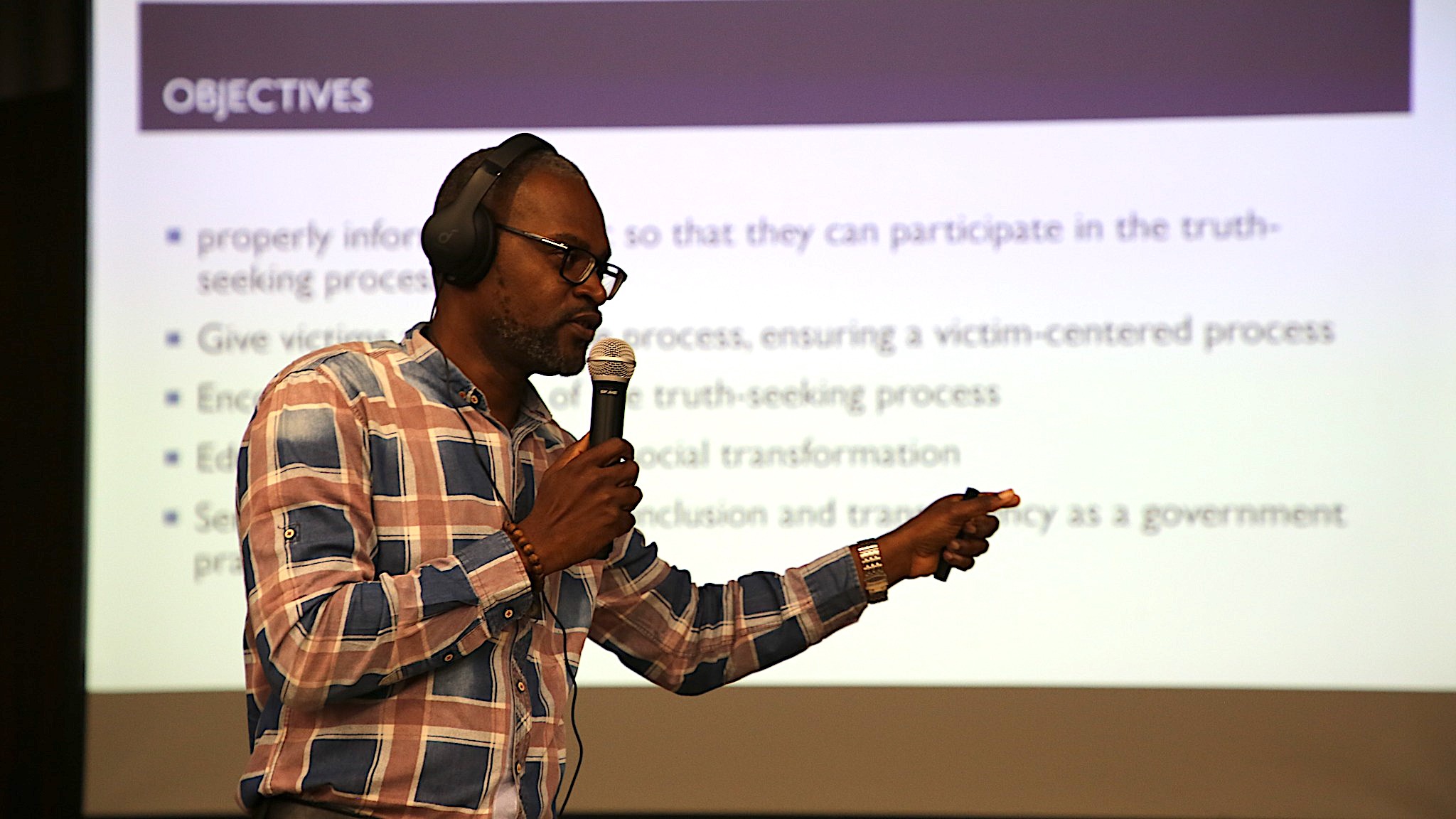 A man stands before a screen with a presentation holding a microphone.