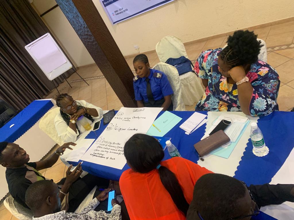 Seven participants in a workshop sit around a table brainstorming ideas on a large piece of paper.