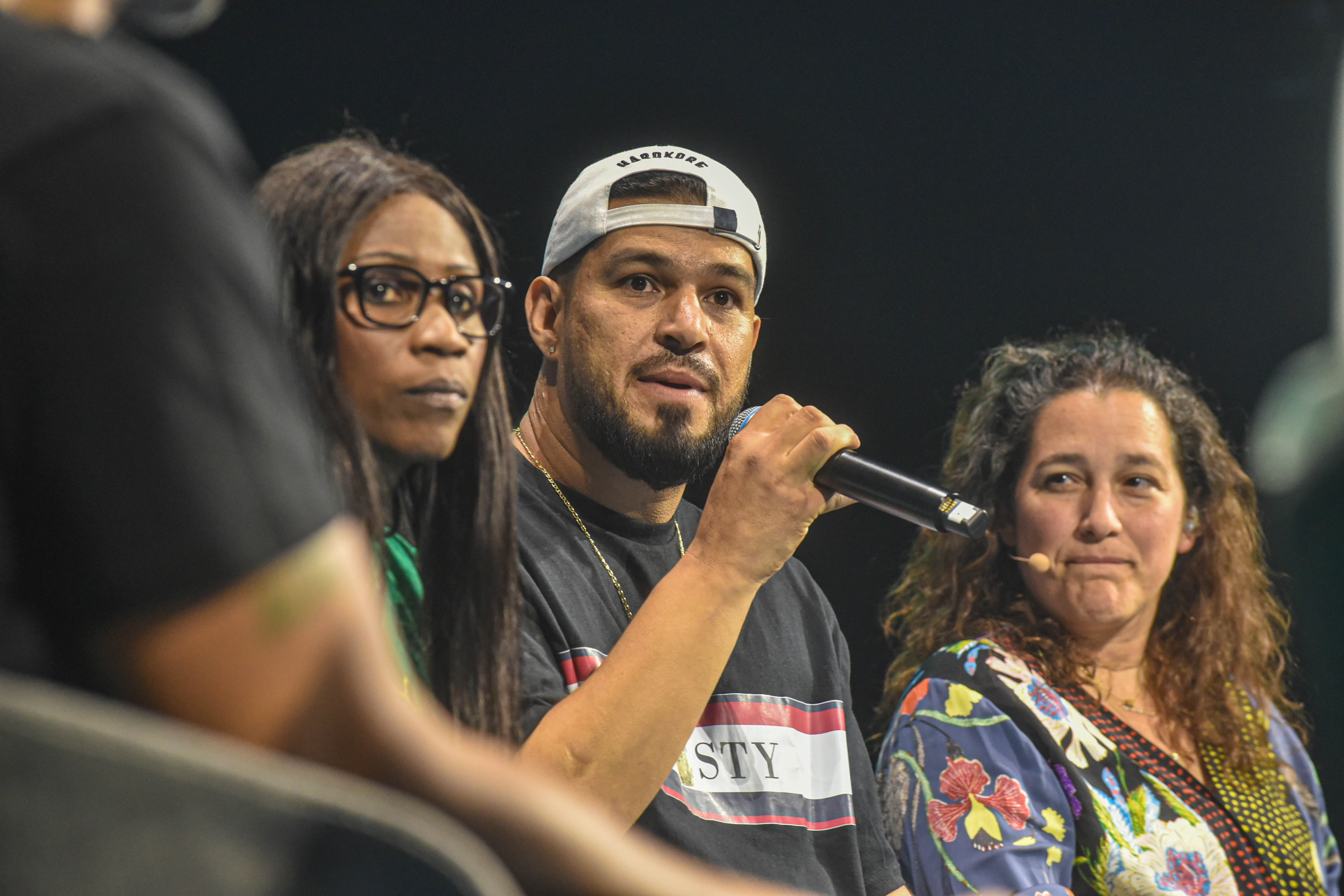 A close-up photo of a man holding a microphone seated between two women.