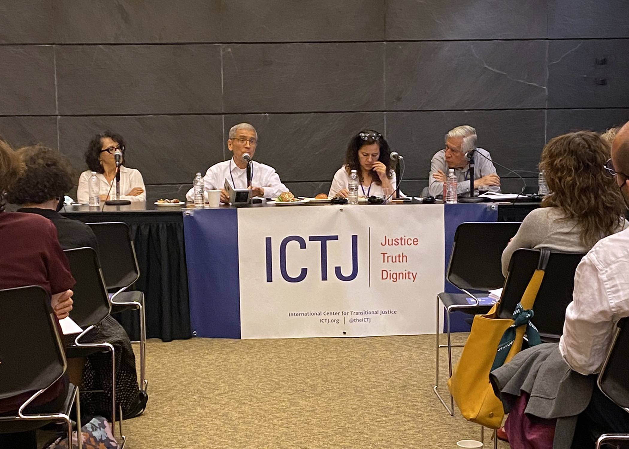 Quatre personnes sont assises à une table avec des microphones face à un public dans une pièce.