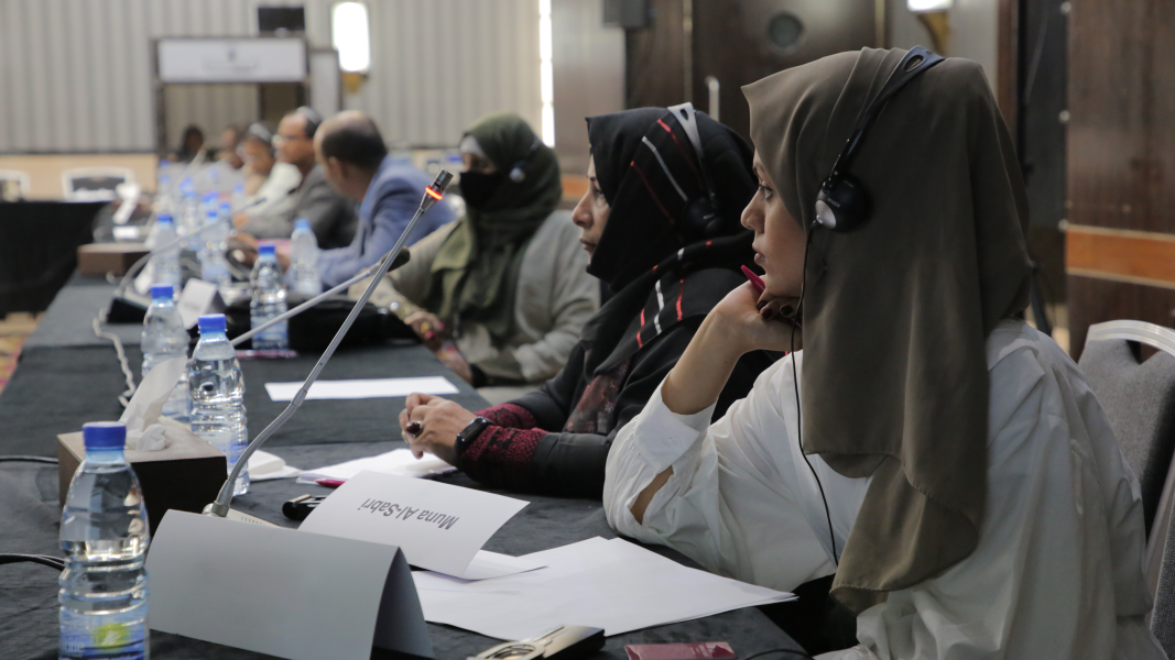 Two women sits at conference table in front of a microphone.