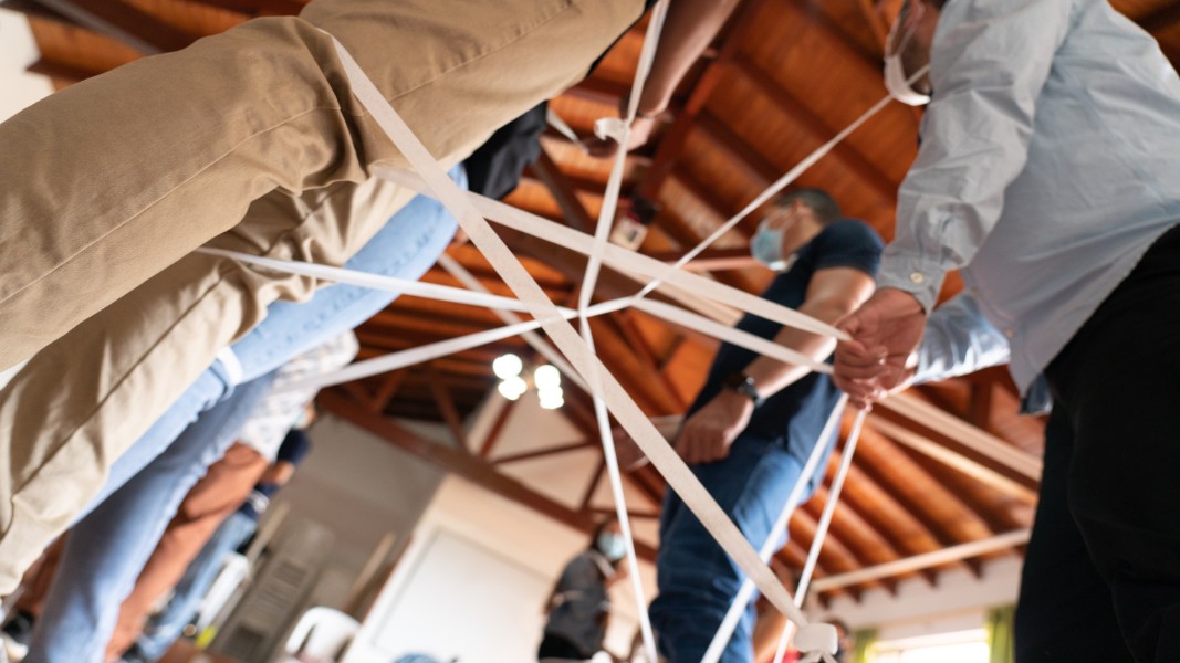 Several people standing some distance apart in a room are bound together by thick bands of while tape.