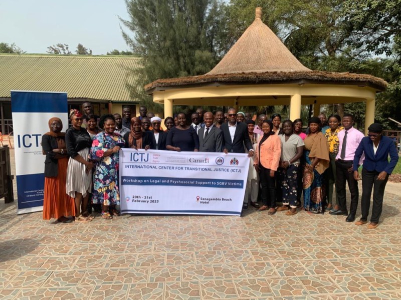 A group of people stand outside behind a banner announcing an ICTJ workshop in the Gambia.