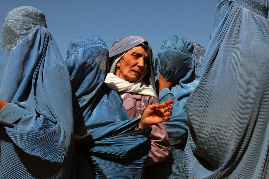 A group of women stand together, four of them wearing full face coverings, or abayas, one with her face uncovered