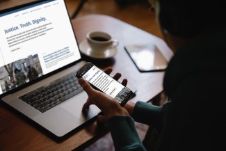 A woman holds a cell phone and looks at a computer screen with ICTJs new website on it