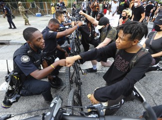 Three police officers kneel with several protesters at a demonstration.