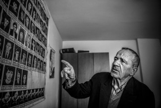 Un hombre señala fotografías de personas que cubren la pared de una habitación.