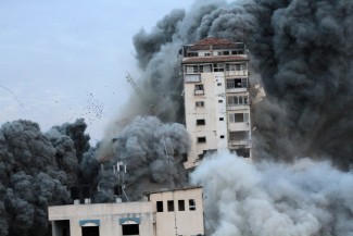 A seriously damaged high-rise building is engulfed in smoke and flames and teeters on the brink of collapse. 