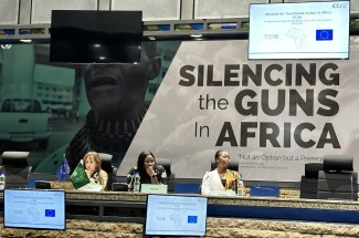 Three women sit side by side at large desk on a podium facing toward an audience.