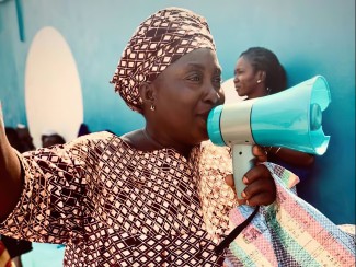 A women in colorful African dress holds a megaphone to her mouth