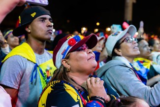 Two women and a man stand in a crowd of people at a protest.